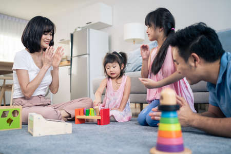 Asian happy family sit on floor, play kid toy together in living room. Attractive parents mother and father spend time with young little girl daughters in house. Activity relationship at home concept.の写真素材