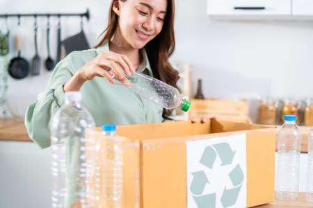 Asian beautiful woman separating trash for further recycling at home. Attractive female put plastic bottles into recycle box for ecologically friendly and saving the environment. Zero waste concept.の写真素材