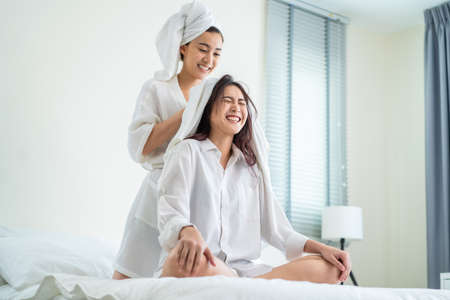 Asian beautiful lesbian couple spending morning leisure time together. Attractive romantic girl in pajamas drying girlfriend's hair after shower on bed in bedroom in house. Homosexual-LGBTQ concept.の写真素材