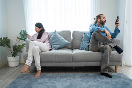 Caucasian phone addict couple don't pay attention with each other. Family problem, New marriage man and woman partner sit on sofa and using smartphone, ignore husband and wife in living room at home.の写真素材