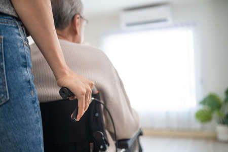 Asian daughter support old disabled man sitting on wheelchair at home. Beautiful girl help and take care of senior elderly mature handicap father patient doing physical therapy in living room in houseの写真素材