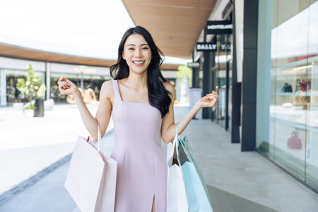 Portrait of Asian attractive girl shopping outdoor in department store. Beautiful woman holding shopping bags then walking alone with happiness, enjoy purchasing in shopping mall and look at camera.の写真素材