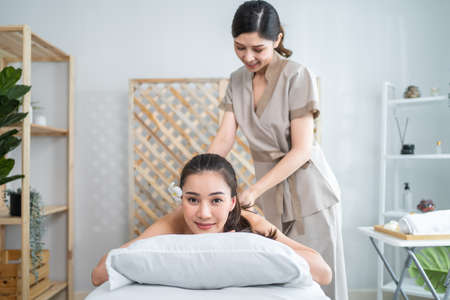 Asian young woman feeling happy and relax during back massage with oil. Attractive beautiful girl lying on massage table, getting physiotherapy from masseuse for skin and body care in spa beauty salonの写真素材