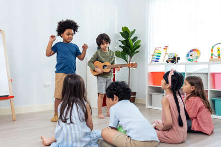Group of Mixed race young little kid playing guitar in schoolroom. Child girl and boy student  spend time play music sing a song and dancing while break with feeling fun together in classroom at schooの写真素材