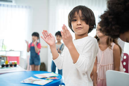 Portrait of Asian cute child boy standing clapping hands in classroom. Student young little kid boy applaud to answer questions in schoolroom enjoy to study with smiling and look at camera at school.の写真素材