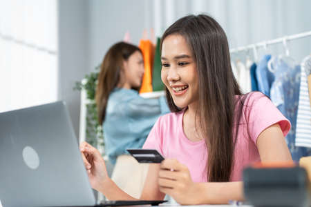 Asian two beautiful women use laptop computer for shopping product sell online. Attractive beautiful girl hold credit card in hand buying and purchase goods on website in smartphonの写真素材