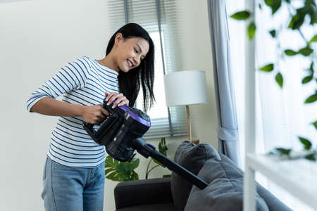 Asian cleaning service woman worker cleaning in living room at home. Beautiful happy girl housewife housekeeper cleaner wear apron and vacuuming messy dirty table for housekeeping housework or chore.の写真素材