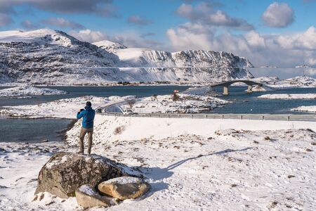 A traveller standing on rock and taking picture of Fredvang village in Lofoten island, Norway,...