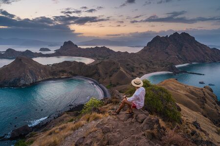 A traveller sitting on top of Padar island and talking picture of beautiful landscape at sunset, Flores island in Komodo national park, Indonesia, Asiaの写真素材