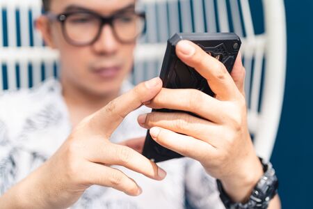 Blurred young Asian man with glasses using smartphone for searching and checking information and communicated to another people. New normal situation. Social distancing concept. Bangkok Thailandの写真素材