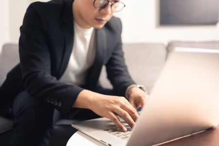 Close up hands of Asian business man using laptop computer working from home sitting on sofa, new normal  digital lifestyle, work from home concept. Bangkok Thailandqqの写真素材