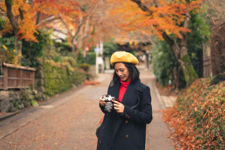 Young happy Asian woman looking to camera for checking picture and walking in beautiful autumn park, Tokyo, Japan, Asia. Lifestyle and travel conceptの写真素材