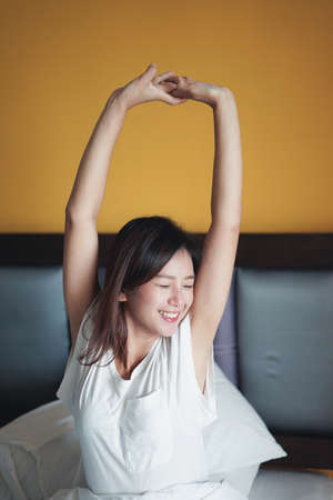 Young beautiful Asian woman smiling and stretching on bed. Positive thinking and lifestyle concept. Bangkok Thailandの写真素材