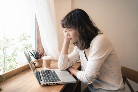 Young Asian worker woman working with laptop computer. A woman thinking of some idea and feeling stress while working from home. Social distancing concept. Bangkok, Thailandの写真素材