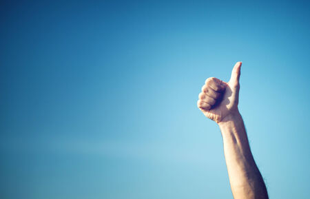 Hand showing thumbs up against pure blue skyの写真素材