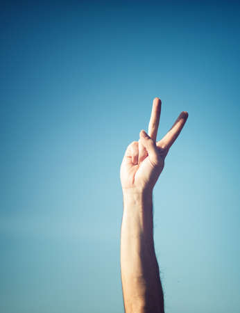 Hand showing peacy victory sign against pure blue sky