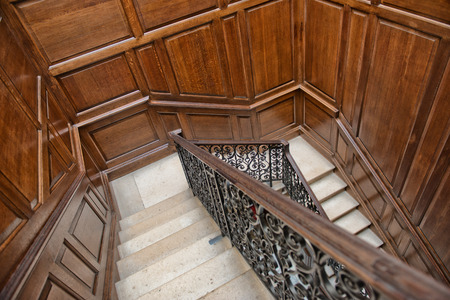 Winding interior staircase with wood paneling on the walls and an ornate wrought iron and oak bannister viewed looking down the treads from aboveのeditorial素材