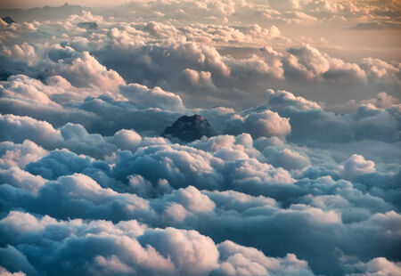 Overview of Peak of Mountain Poking Through Clouds as if seen from Airplaneの写真素材