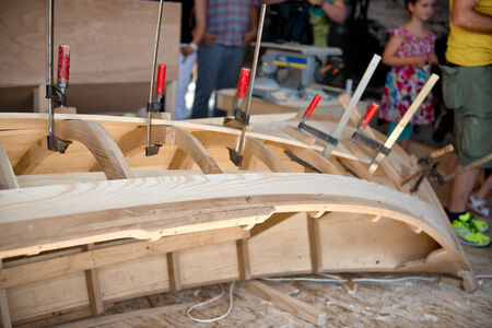 Wooden boat being made at the Danube Festival in Ulm with a view of the open hull structure on a workshop floor with the lower body of a few spectators visible behindのeditorial素材