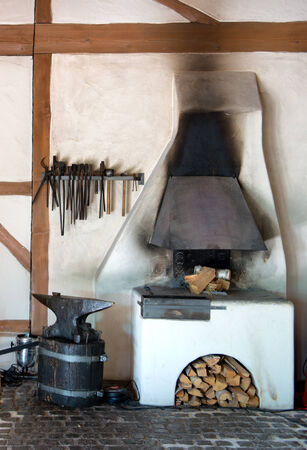 Rustic interior in an old forge with a wood burning oven, tools hanging on the wall and old metal anvilのeditorial素材