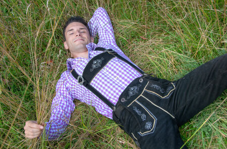 Young man in traditional Bavarian clothes relaxing in the fieldの写真素材