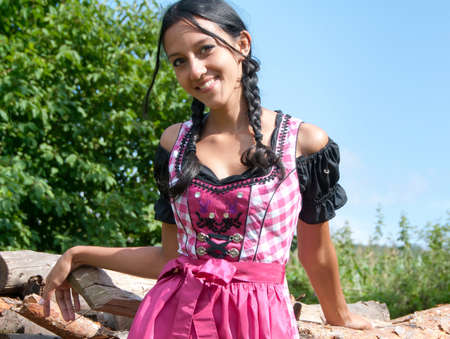 Young woman in dirndl posing in front of a pile of logsの写真素材