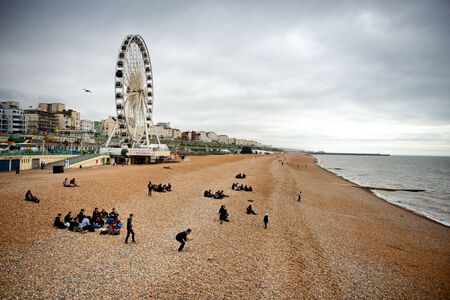 View down the golden sand of Brighton beachfront to the ferris wheel and amusement park with groups of people on the beachのeditorial素材