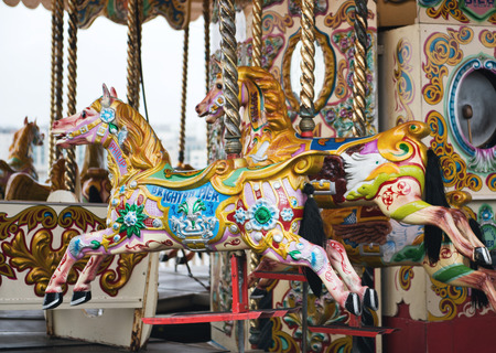 Brightly painted horses on a vintage carousel or merry-go-round at a fairground for children to ride as they go round and up and down imitating gallopingのeditorial素材