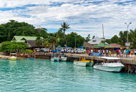 People walking on the quay at La Digue harbor in the Seychelles with several pleasure boats moored alongsideのeditorial素材
