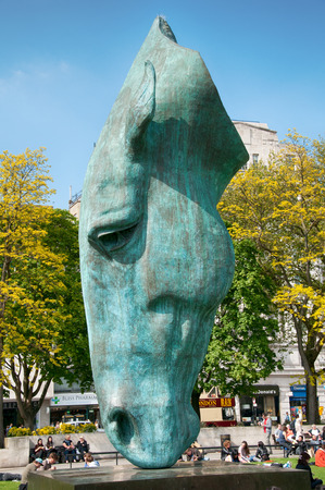 Statue of a horse head by Nic Fiddian-Green in Hyde Park, London patinated by green verdigris with people relaxing on the green grass surrounding itのeditorial素材