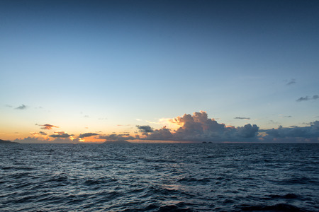 Colorful orange tropical sunset behind cumulonimbus clouds towering above a calm blue oceanの写真素材