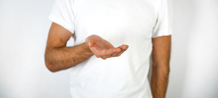Man holding out his empty cupped hand and palm in a product placement, giving, showing or request gesture and concept over his white t-shirt, close up viewの写真素材