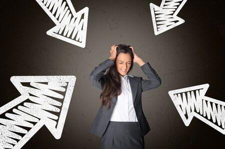 Frustrated Young Businesswoman Tearing her Hair Surrounded by Conceptual White Arrows on Abstract Gray Gradient Background.の写真素材