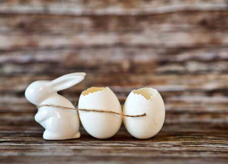 Close up Small Easter Bunny Figurine Pulling Broken Egg Shells Using a String on Top of a Wooden Table with Blurry Background.の写真素材