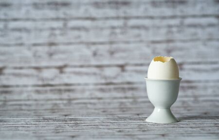Close up Cracked White Egg in a Ceramic Cup on Top of a Wooden Table with Fuzzy Background,...