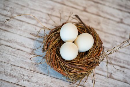 Aerial View of Chicken Nest with Three Whole Eggs on Top of a White Wooden Table.の写真素材