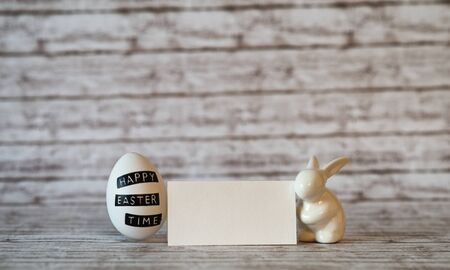 Blank Small Greeting Card with White Printed Easter Egg and Small Rabbit Porcelain on Top of a Table with Fuzzy Background.の写真素材