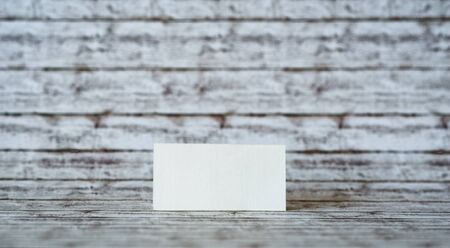 One Blank Rectangular Greeting Card Standing on a Wooden Table with a Vintage Wall Background.の写真素材