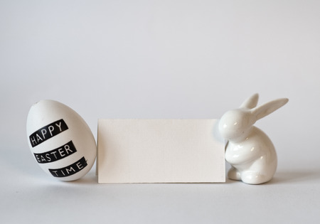 Blank Horizontal Card Framed by Easter Egg with Typed Message and White Rabbit Figurine on White Backgroundの写真素材