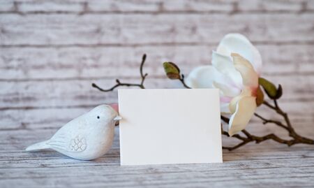 Small White Bird Figurine with Horizontal Blank Card with Copy Space for Personal Message and White Blossoms on Rustic White Wooden Backgroundの写真素材