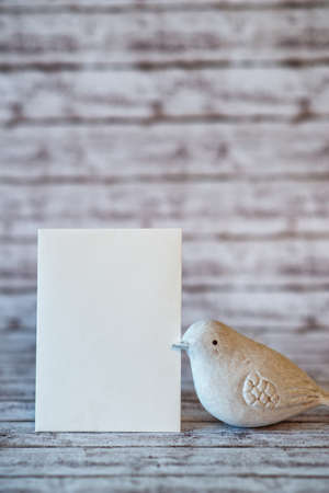 White Bird Figurine with Blank Vertical Card on Rustic White Wooden Background with Copy Space for Personal Message or Greetingの写真素材