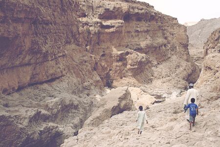 Father walking with his sons in the gorge of the Wadi Bani Khalid near Muscat Oman traveling on foot through the rocky barren terrain above the perpetual streamの写真素材