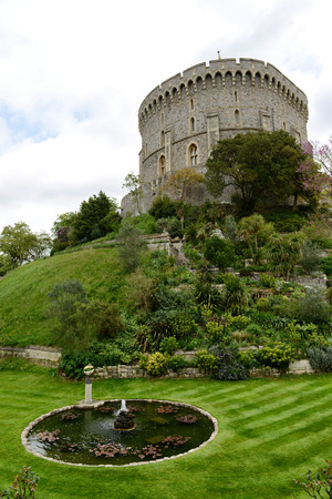 Round pond in the formal park at Windsor Castle, Berkshire, UK with an ancient medieval stone tower of the castle visible over the vegetation on the rockeryのeditorial素材
