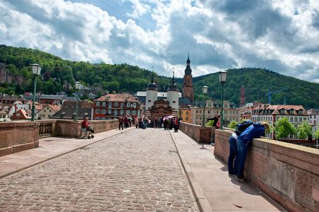 Crowd of Tourists on Cobblestone Street of Old Bridge Leading to Old Town Heidelberg in the Lush Green Foothills of Baden-Wurttemberg, Germanyのeditorial素材