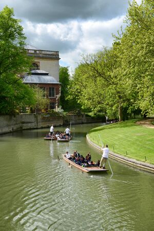 People punting on the river in Cambridge rowing away from the camera around a bend in the river past historical buildings amongst lush green treesのeditorial素材