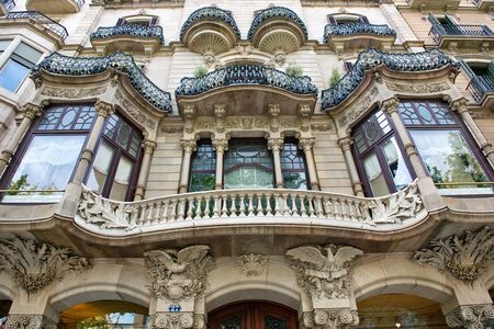 Detail of an Art Nouveau building facade in Barcelona, Spain with a curved balcony between symmetrical windows and ornate stone carving and sculpturesのeditorial素材