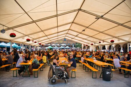 View of a Bavarian styled Oktoberfest in Barcelona, Spain taking place in an undercover marquis with rows of benches and people and a wheelchair in the foregroundのeditorial素材