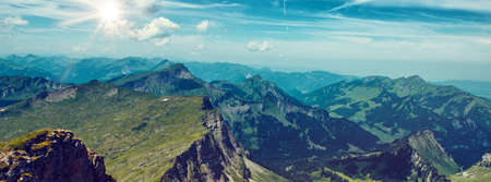 Panoramic Scenic View of Expansive Green Mountain Range with Bright Sun and Blue Skyの写真素材