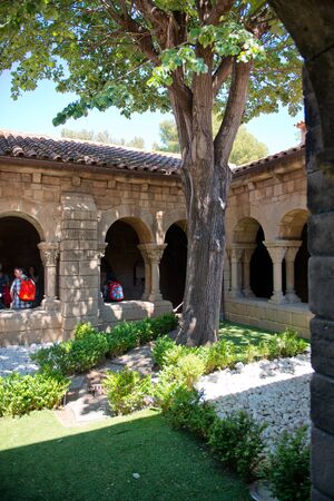 Inner courtyard with trees and a garden surrounded by an arched colonnade with a tourist visible walking through in Espanyol Poble, Barcelona, Spainのeditorial素材