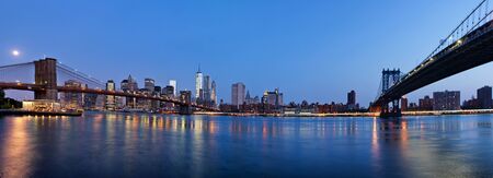 Panoramic View of Manhattan and Brooklyn Bridges Spanning East River with Illuminated Skyline View of New York City in the Eveningの写真素材